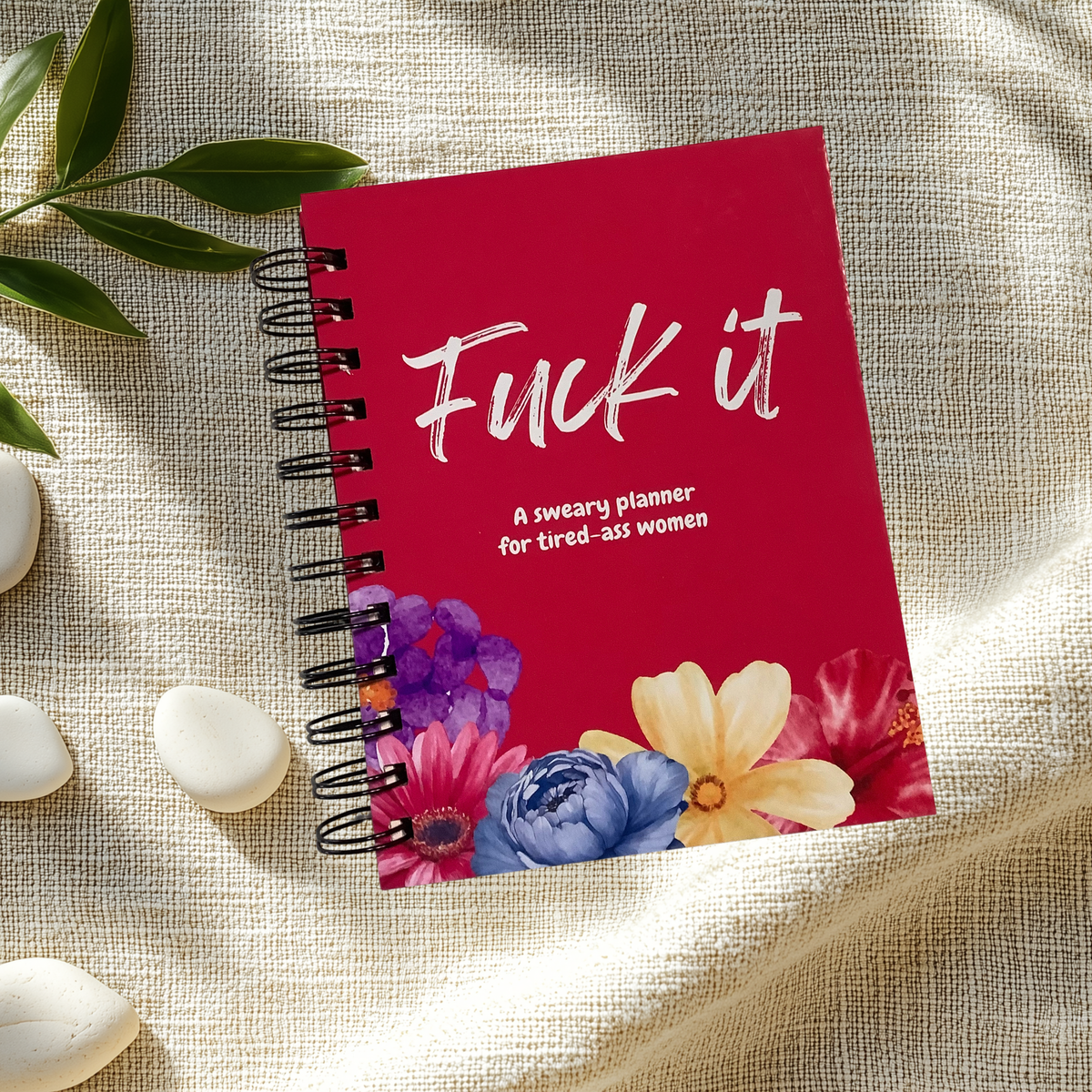 Spiral-bound planner with a red floral cover reading “Fuck it. A sweary planner for tired-ass women.”