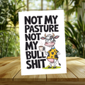 White aluminum sign with a unimpressed cartoon cow in a yellow shirt holding a steaming mug, reading “Not my pasture, not my bullshit.”