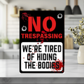 Black, red and white sign with bullet-hole graphics and red splatters, reading “No trespassing. We’re tired of hiding the bodies.”