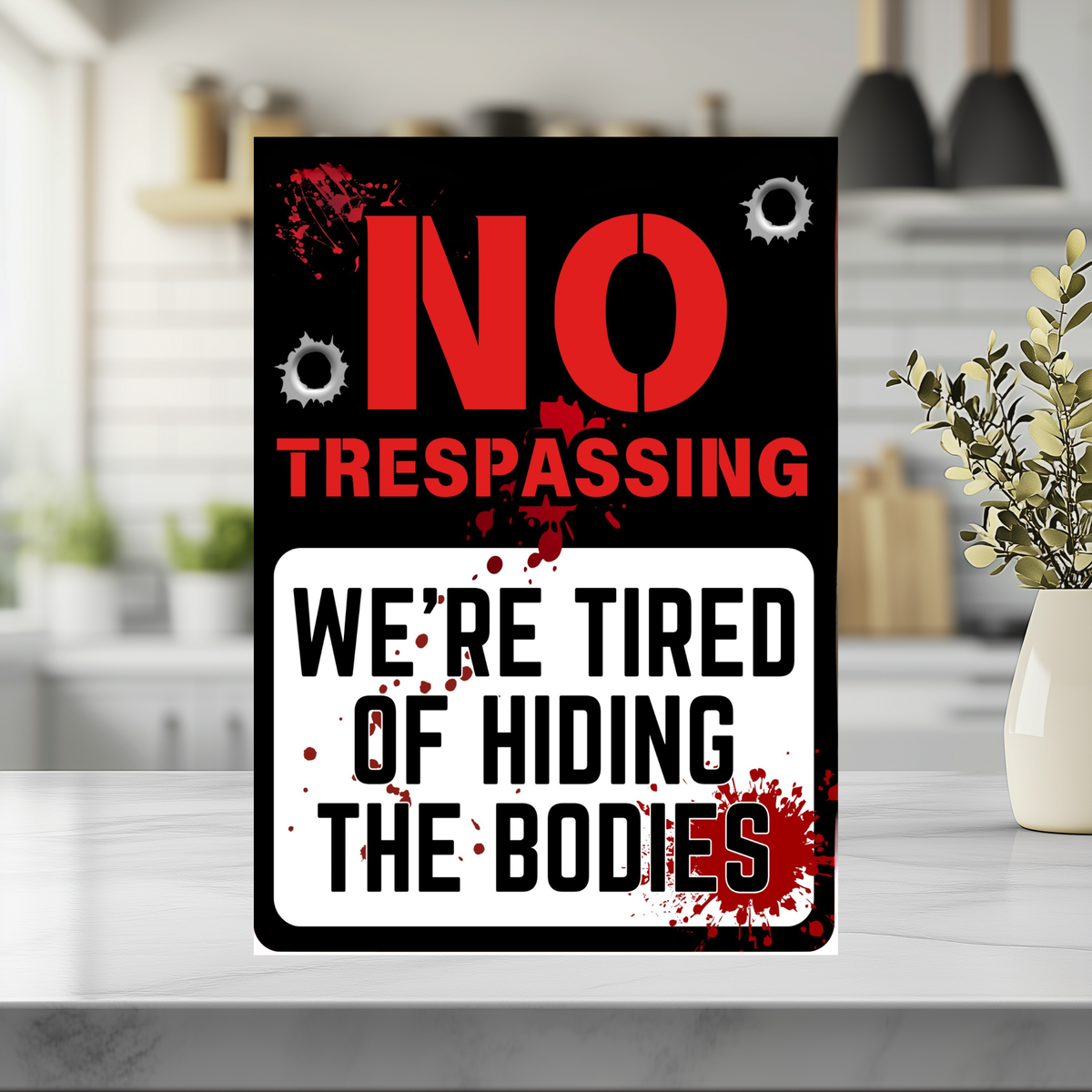 Black, red and white sign with bullet-hole graphics and red splatters, reading “No trespassing. We’re tired of hiding the bodies.”