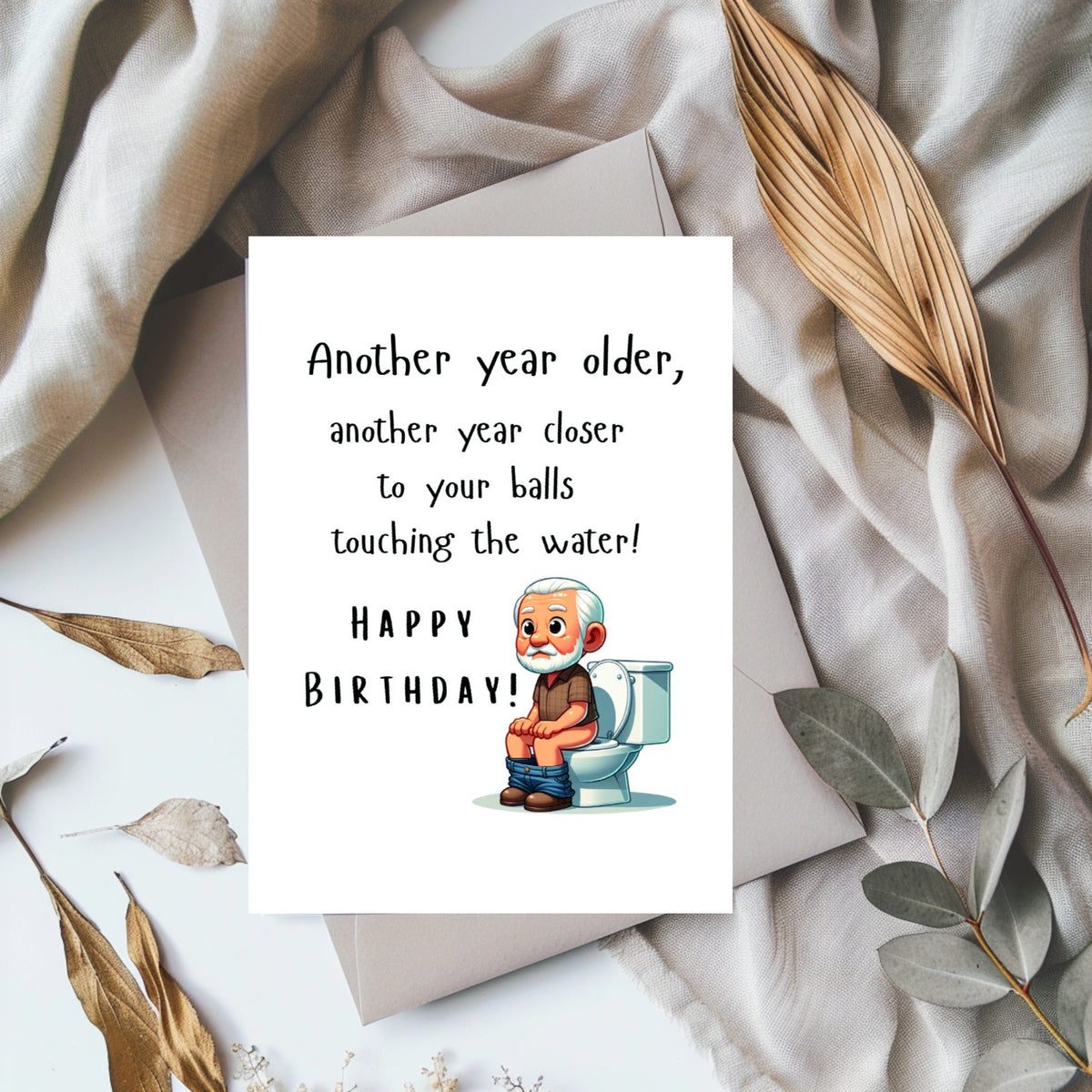 White rectangular birthday card with a cartoon older man sitting on a toilet, reading “Another year older, another year closer to your balls touching the water! Happy Birthday!”