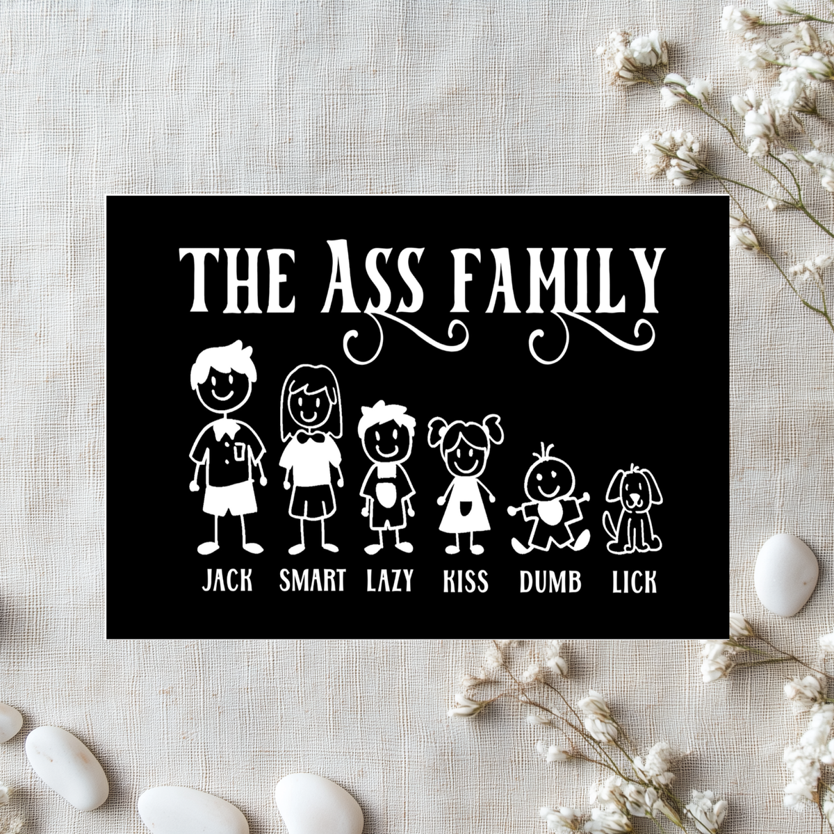 Black aluminum sign reading “The Ass Family,” with white cartoon family members and a dog labelled “Jack,” “Smart,” “Lazy,” “Kiss,” “Dumb” and “Lick.”
