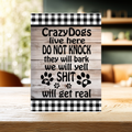 Wood-look aluminum sign with black-and-white checked borders and paw prints, reading “Crazy dogs live here. Do not knock. They will bark, we will yell, shit will get real.”