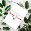 White rectangular card reading “Here’s one coupon for Hawk Tuah,” with red script lettering and a black striped heart.