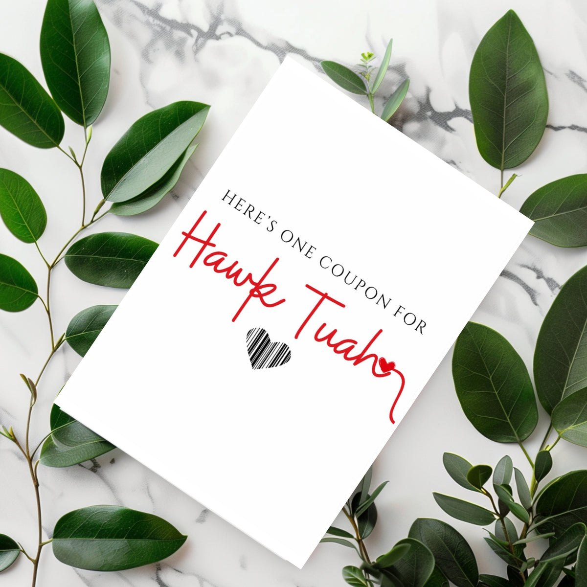 White rectangular card reading “Here’s one coupon for Hawk Tuah,” with red script lettering and a black striped heart.