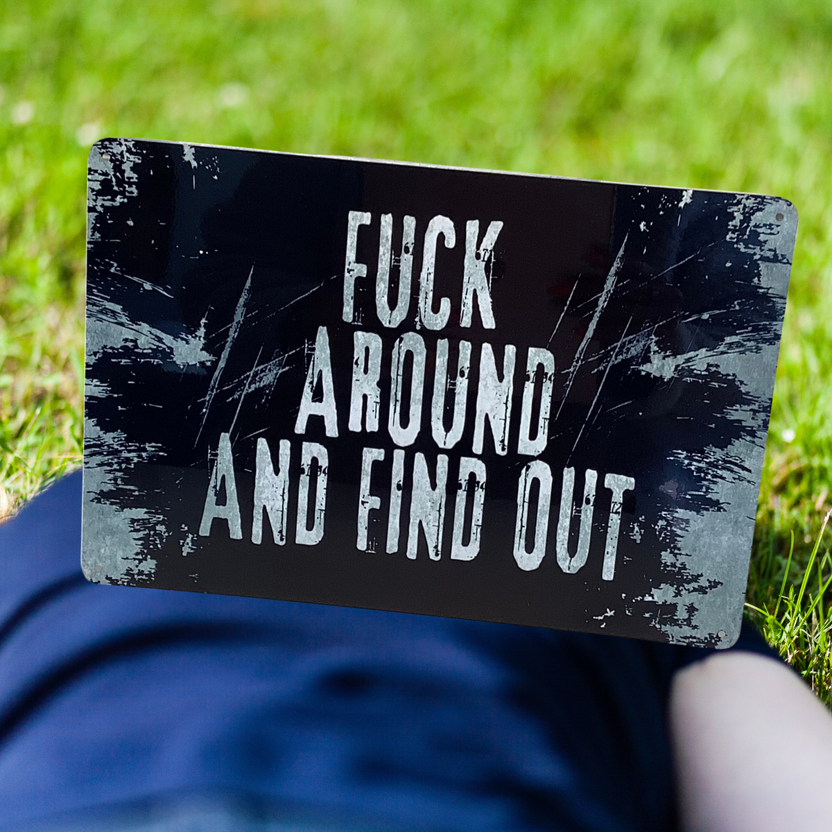 Black aluminum sign with distressed white lettering and scratched-edge graphics, reading “Fuck around and find out.”