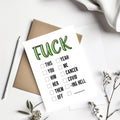 A white novelty greeting card with the word 'FUCK' in large green outlined letters at the top, followed by a checklist of phrases including 'THIS', 'YOU', 'HIM', 'HER', 'THEM', 'ME', 'YEAH', 'CANCER', 'COVID', 'ING HELL', and 'OFF'. The card is styled in a flat lay with a brown kraft envelope, a silver pen, white fabric, and small dried flowers on a white background.