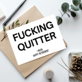A white greeting card with bold black text reading 'FUCKING QUITTER' and smaller text 'I MEAN, HAPPY RETIREMENT,' styled on top of a kraft envelope with eucalyptus leaves, a pen, and other flat-lay props on a white surface.