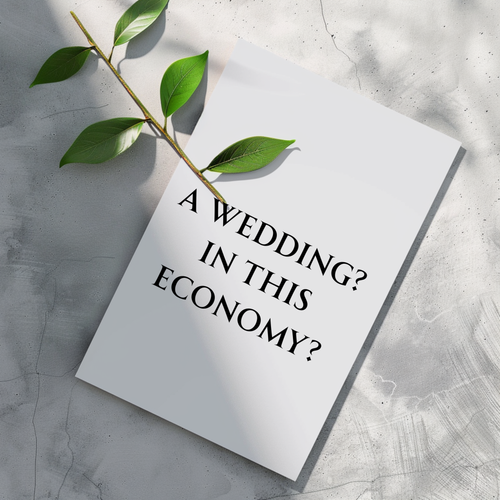 A white rectangular card or print with the text 'A WEDDING? IN THIS ECONOMY?' in black serif lettering, placed on a light gray textured surface with a green leafy stem across the top left.