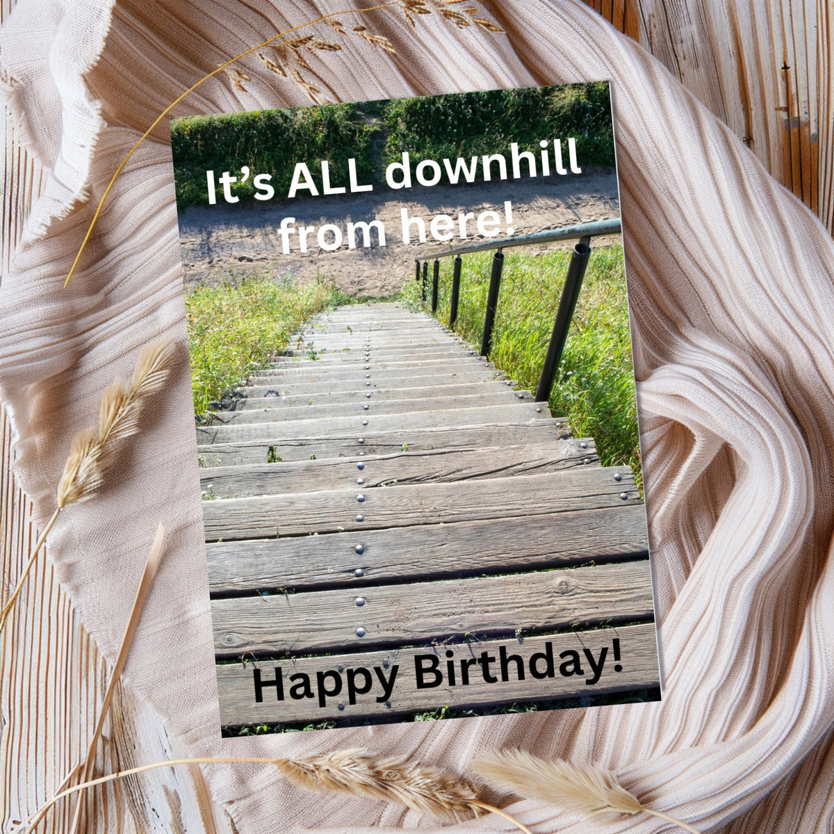 Rectangular birthday card showing wooden steps descending a grassy hillside, reading “It’s ALL downhill from here!” and “Happy Birthday!”