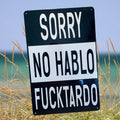 Black and white aluminum sign with bold lettering reading “Sorry, no hablo fucktardo.”