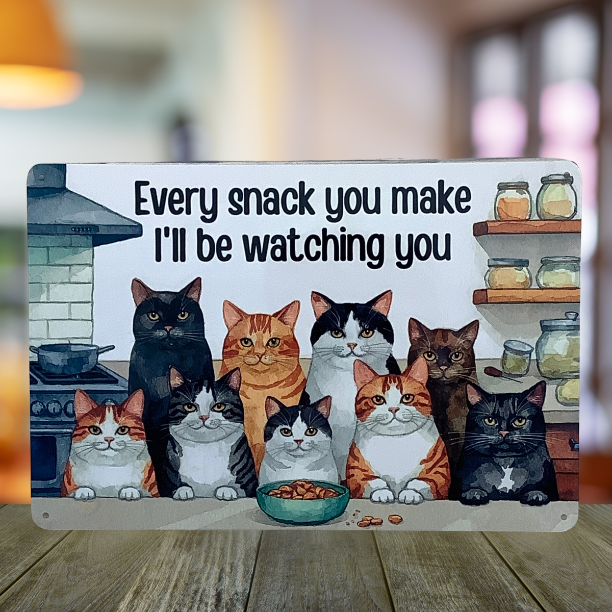 Aluminum sign displayed on a wooden table, featuring nine cats around a snack bowl and the words “Every snack you make, I’ll be watching you.”