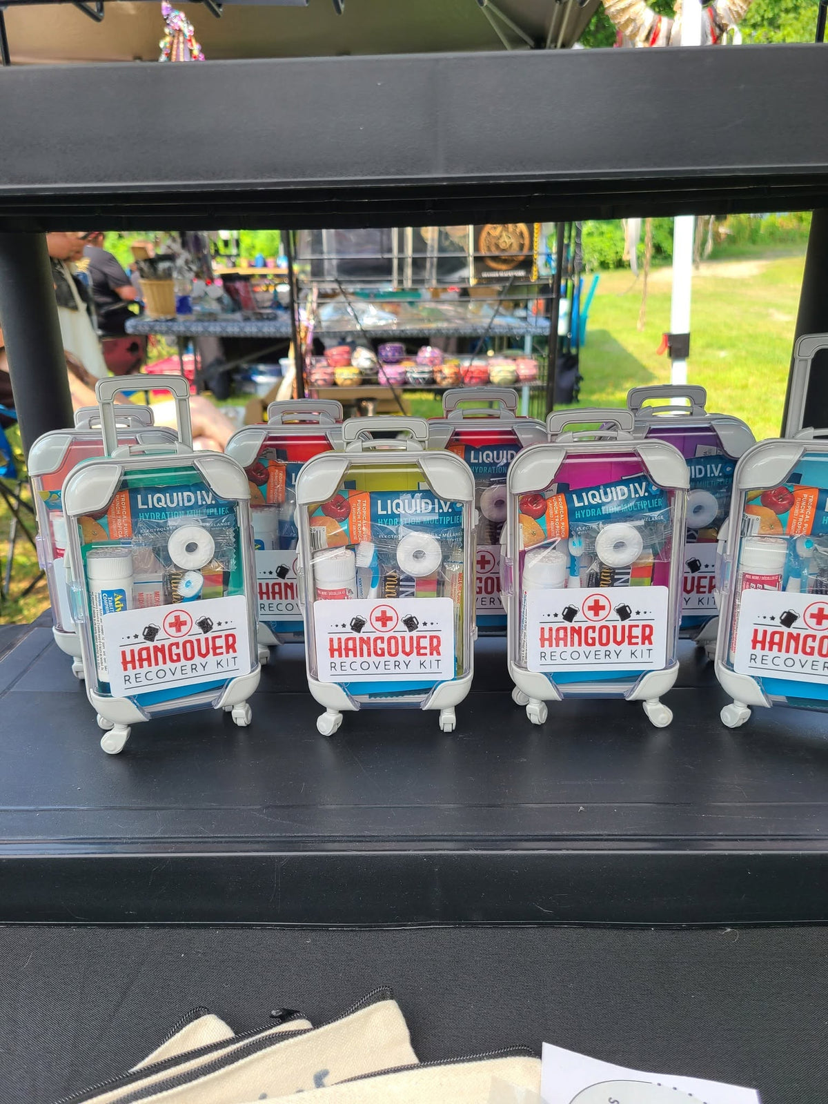Hangover kits in colourful miniature rolling suitcases with clear fronts showing their contents and labels reading “Hangover Recovery Kit.”