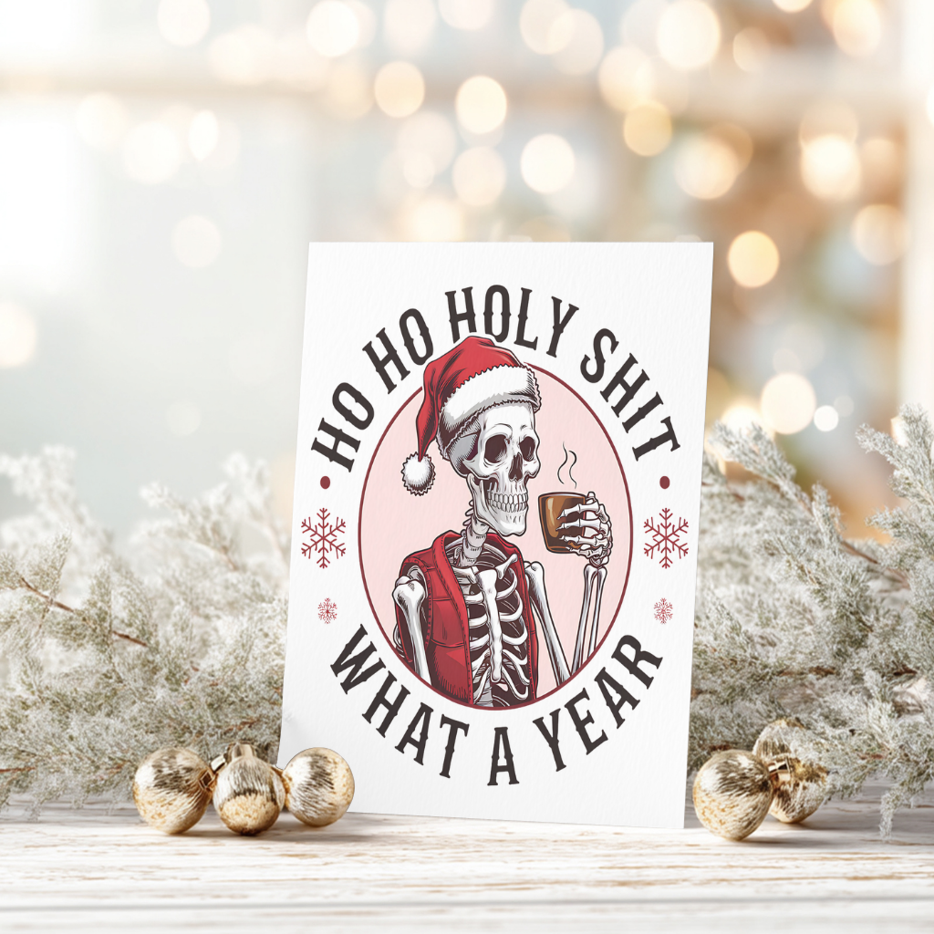 White rectangular Christmas card with a skeleton wearing a Santa hat and red scarf, holding a steaming mug, reading “Ho Ho Holy Shit What a Year.”