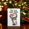 White rectangular Christmas card reading “This year can kiss my,” with a donkey wearing a Santa hat replacing the word “ass.”
