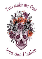 Purple skull decorated with flowers, spiders and webs on a white background, with the words “You make me feel less dead inside.”