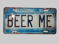 Distressed blue and cream faux license plate sign with large black lettering reading “Beer Me.”