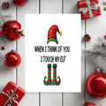 White rectangular Christmas card with a red and green elf hat and striped elf boots, reading “When I think of you I touch my elf.”